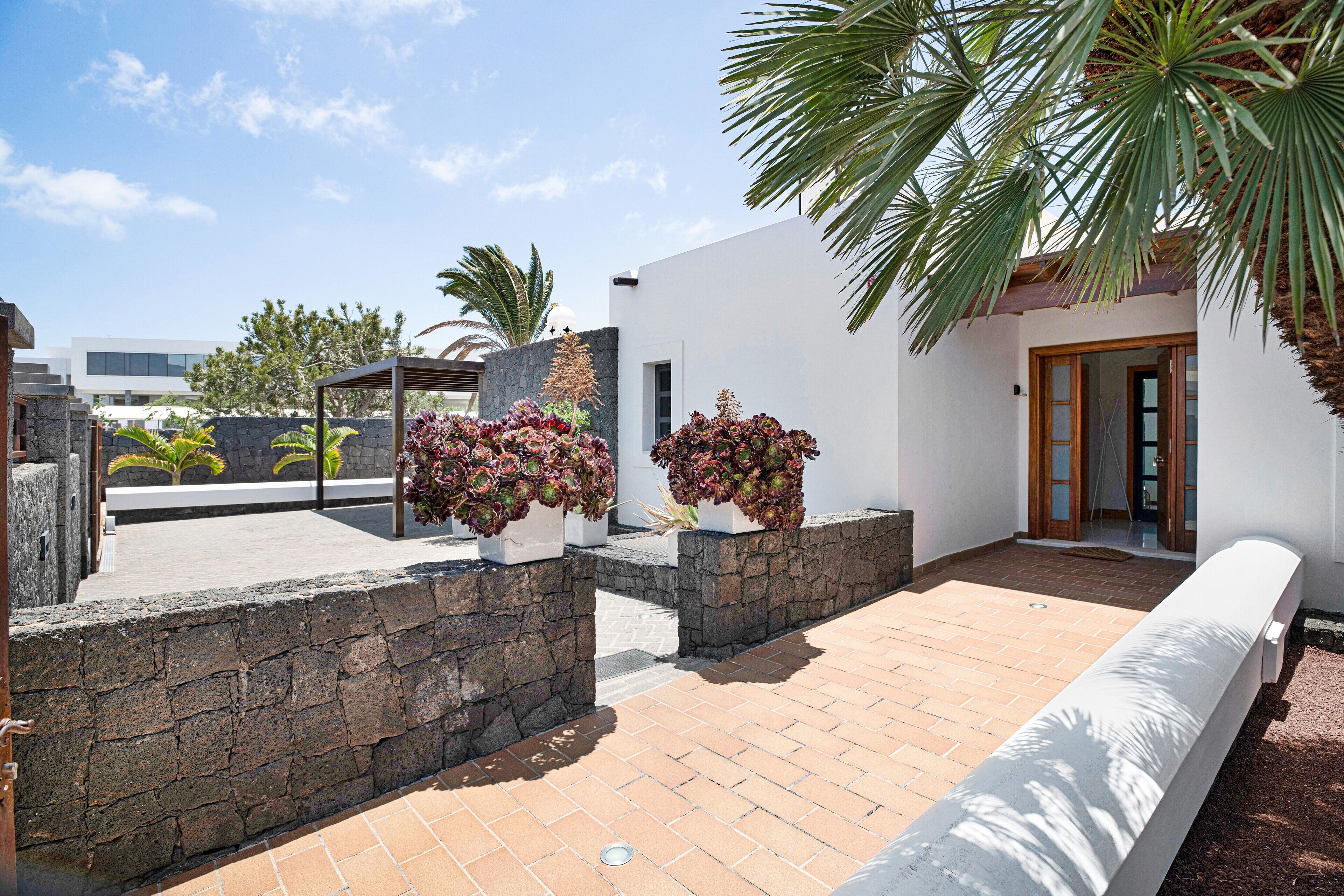 Un patio con pared de piedra, una banca blanca y plantas en macetas.
