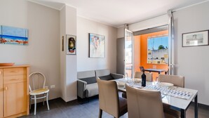 A modern dining area with a table, chairs, and a sofa. There is a window with curtains, a cabinet, and artwork on the walls.