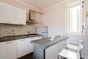 A modern kitchen with white cabinets, a gas stove, a stainless steel range hood, and a window with frosted glass.