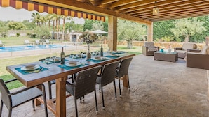 Ein Essbereich im Freien mit einer Holz-Pergola, einem Pool und Liegestühlen.