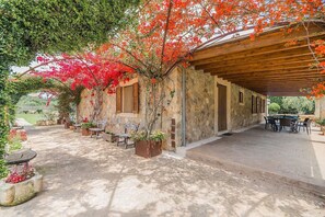 A covered outdoor seating area with stone walls, wooden furniture, and potted plants.