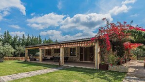 Eine überdachte Terrasse mit Gartenmöbeln, einer Steinmauer und einem Garten mit blühenden Pflanzen.