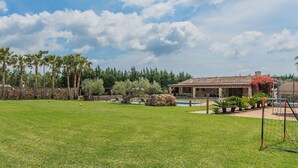 Ein grünes Hinterland mit Pool, Terrasse und einem Gebäude mit Ziegeldach.