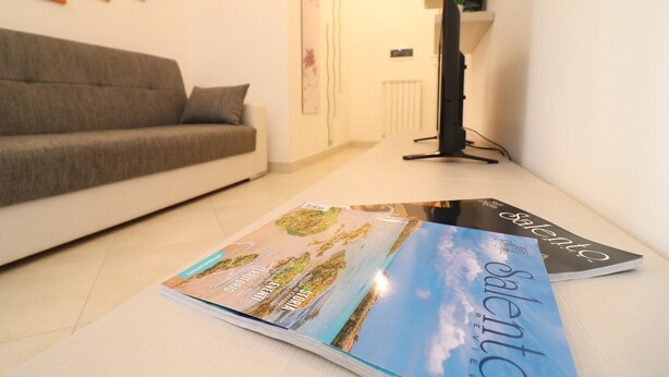 Un salon avec un canapé, un magazine posé sur le sol et un radiateur à l’arrière-plan.