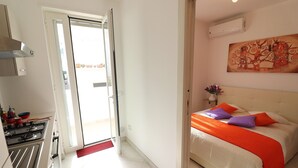 Une chambre avec un lit, un tableau, et un coin cuisine comprenant une cuisinière et des placards.