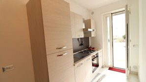 Une cuisine avec des meubles en bois, une cuisinière à gaz et un paillasson rouge à l’entrée.
