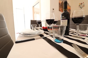 Mesa de jantar posta com copos de vinho, uma garrafa de vinho e talheres.