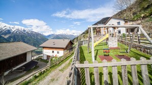 Un village de montagne avec une aire de jeux, une maison en bois et une grange.