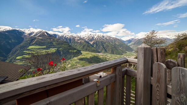 Une terrasse en bois donnant sur un paysage montagneux, avec des sommets enneigés et des vallées verdoyantes.