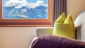 Une pièce avec une fenêtre donnant sur des montagnes enneigées, un canapé gris et une couverture violette.