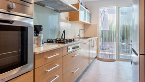 Cozinha moderna com eletrodomésticos de aço inoxidável, armários de madeira e uma porta de vidro deslizante que dá para uma área externa.