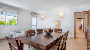 Uma área de refeições com uma mesa de madeira, cadeiras, uma tigela de pinhas e vista para o verde lá fora.