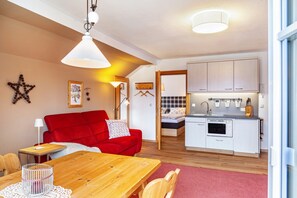 A compact living space with a dining area, a red sofa, a kitchenette, and a bed in the background.