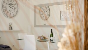 Un coin repas avec deux horloges, un lustre et une table sur laquelle se trouvent une bouteille et des verres.