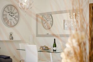 Un coin repas avec deux horloges, un lustre et une table sur laquelle se trouvent une bouteille et des verres.