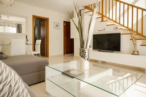 Un salon moderne avec une table basse en verre, un canapé, un téléviseur et un escalier.