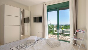 Une chambre à coucher avec un lit, une télévision, un balcon avec une table et des chaises, et une porte verte.