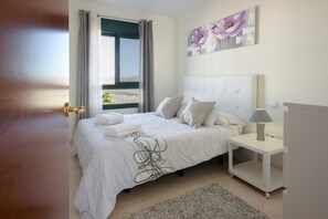 Une chambre à coucher avec un lit, une table de chevet, une lampe, une fenêtre avec des rideaux et un tableau au mur.