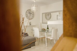 Un coin repas avec une table en verre, des chaises blanches et deux horloges murales.