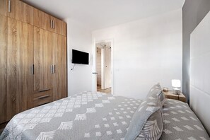 Een slaapkamer met een bed, een houten garderobe, een televisie en een nachtkastje met een lamp.