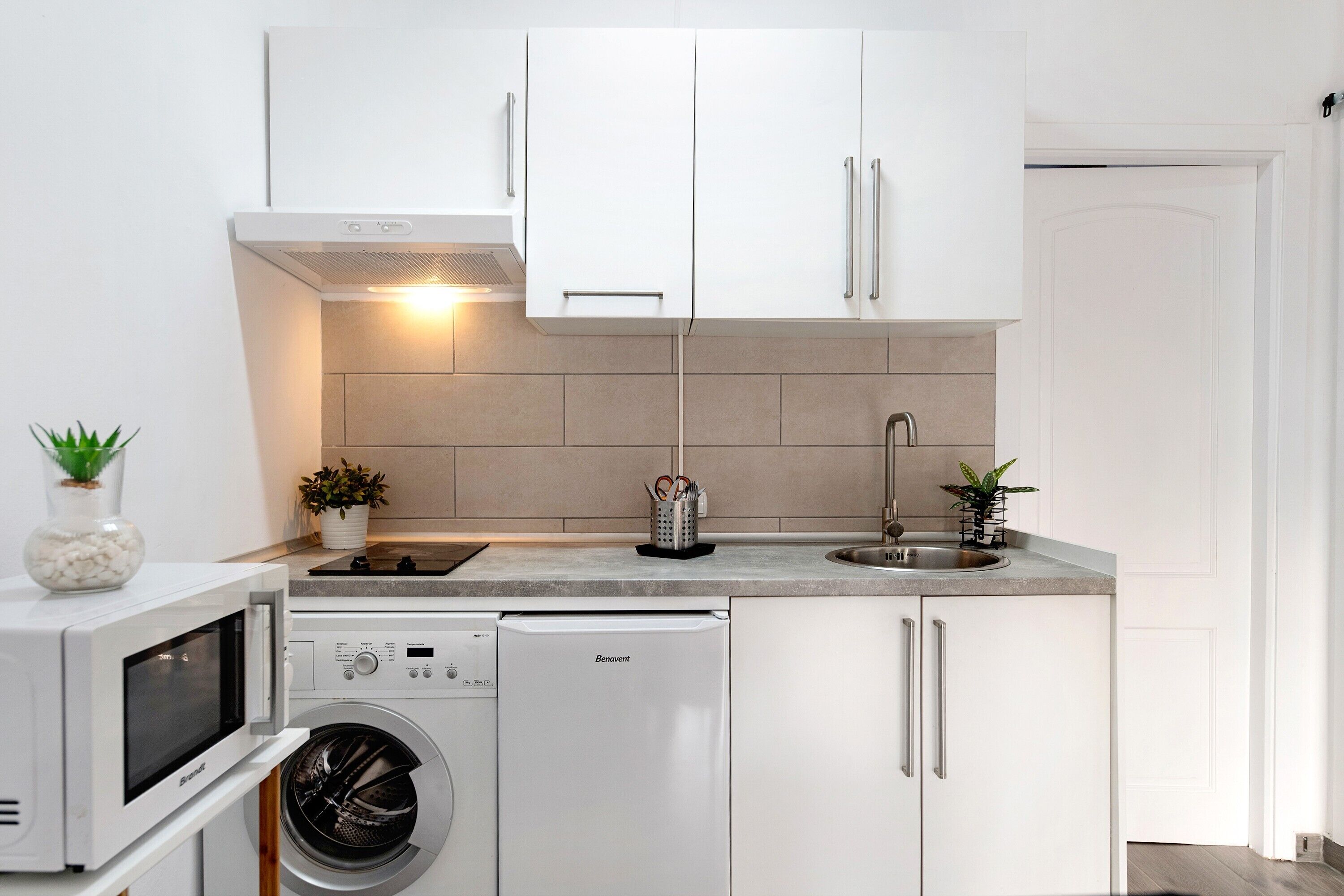 A compact kitchen with white cabinetry, a built-in microwave, a dishwasher, and a sink.