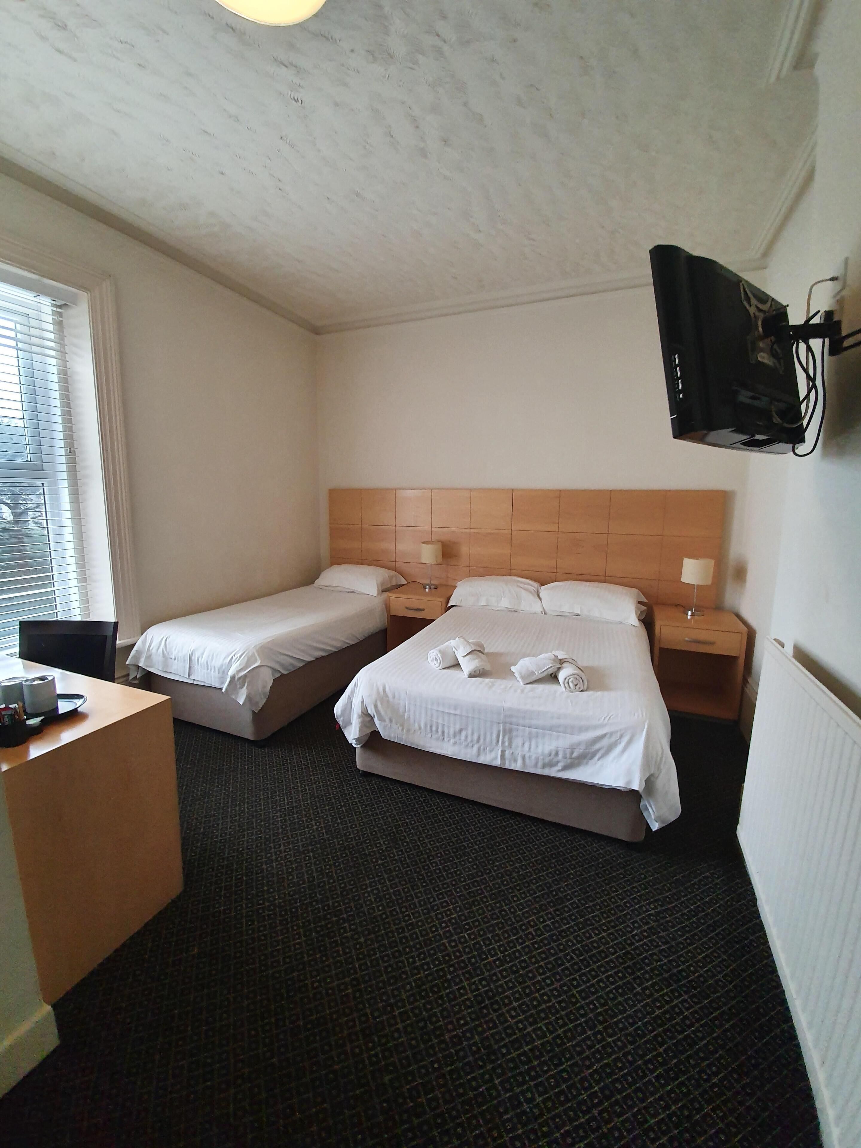A hotel room with two beds, a desk, and a TV mounted on the wall.