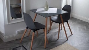 Un coin repas comprenant une table et quatre chaises, un petit tapis et une fenêtre avec des stores.