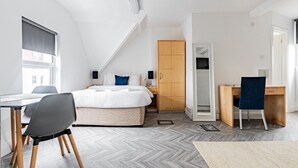 Une chambre moderne comprenant un lit, un bureau et une chaise, avec un parquet à motifs en chevrons et une armoire en bois.