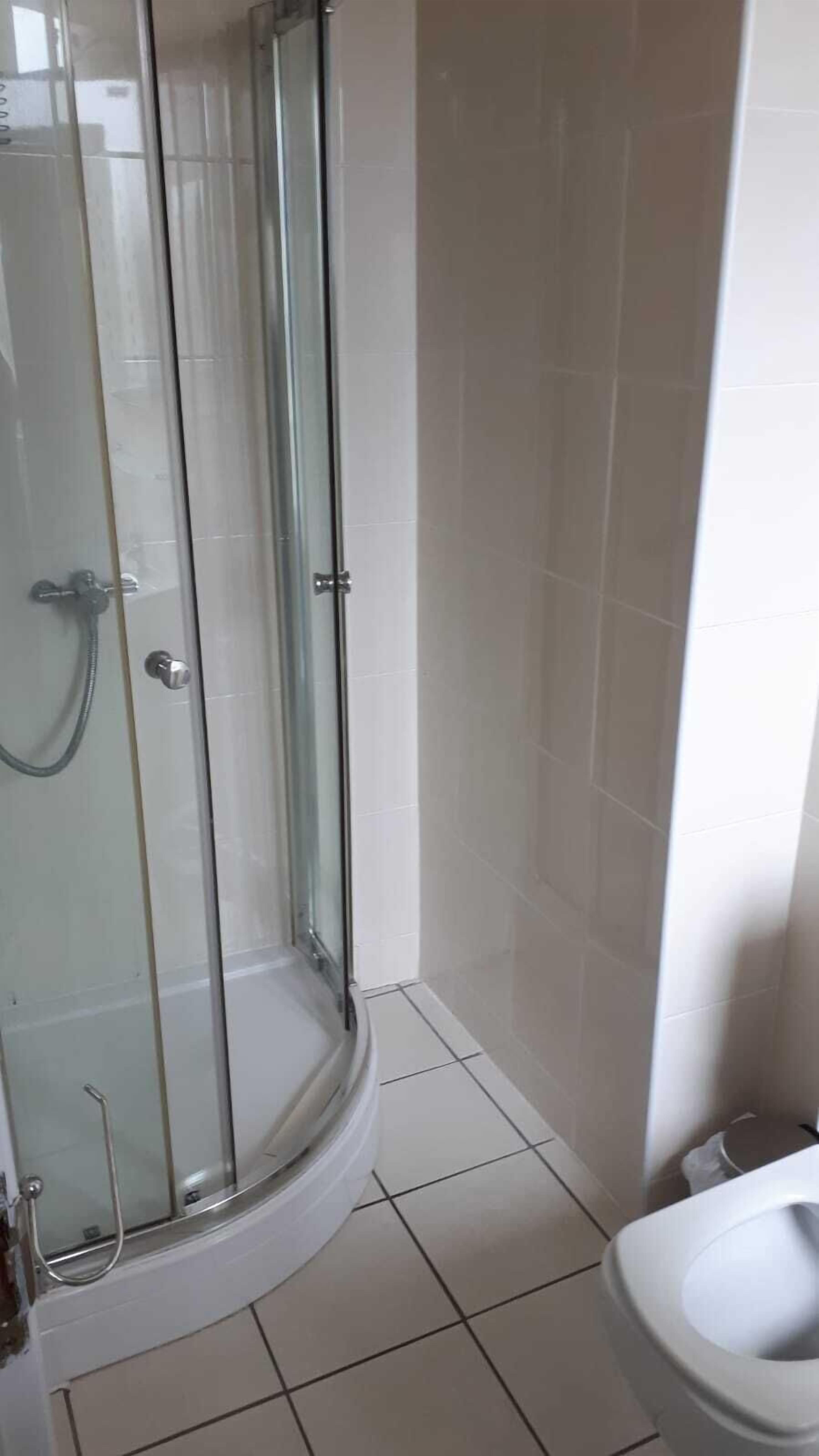Et badeværelse med glasvæg omkring brusenichen, hvide flisemure og et hvidt toilet.