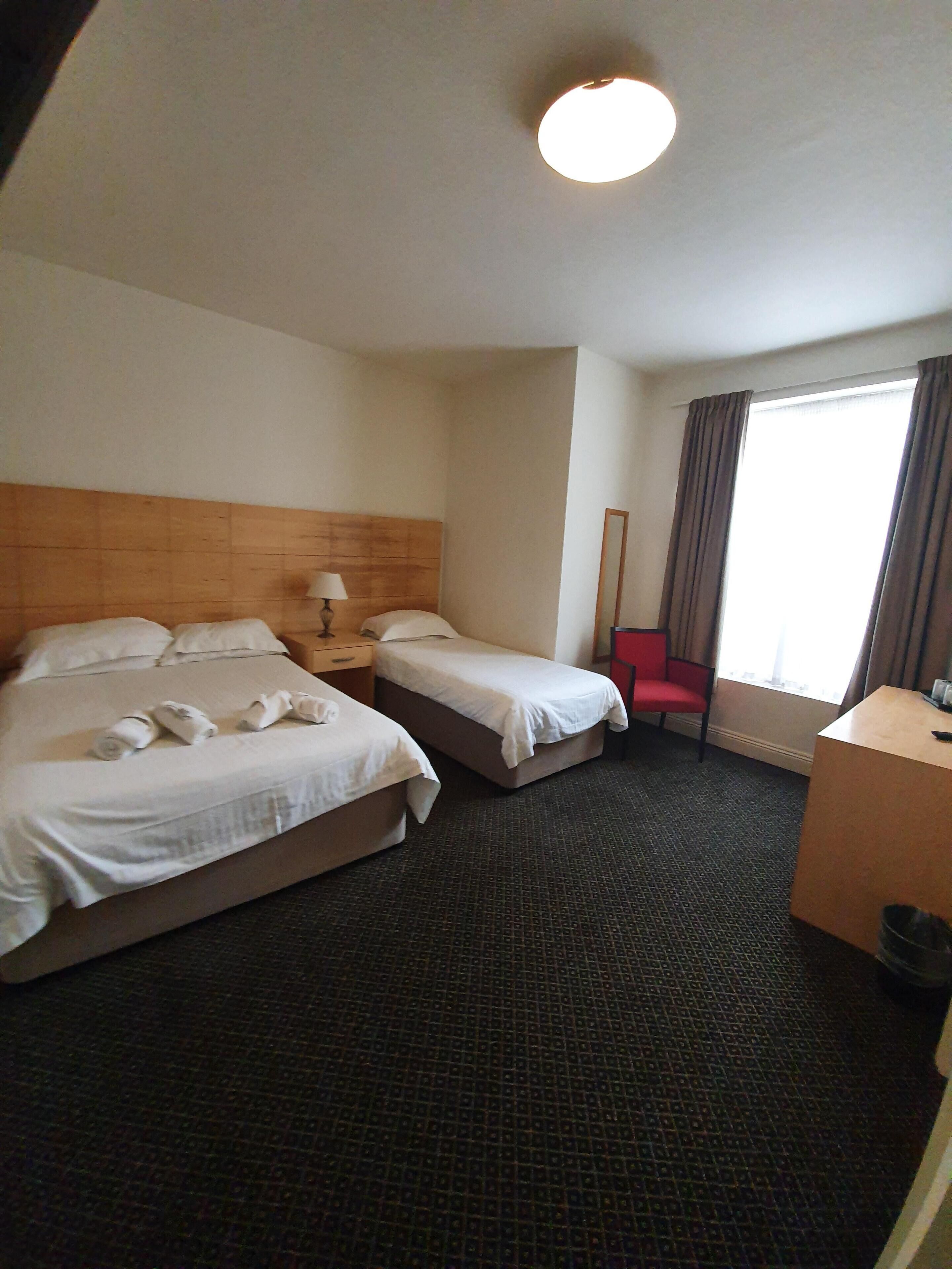 Habitación de hotel con dos camas, un escritorio, una silla y un ventanal con cortinas.