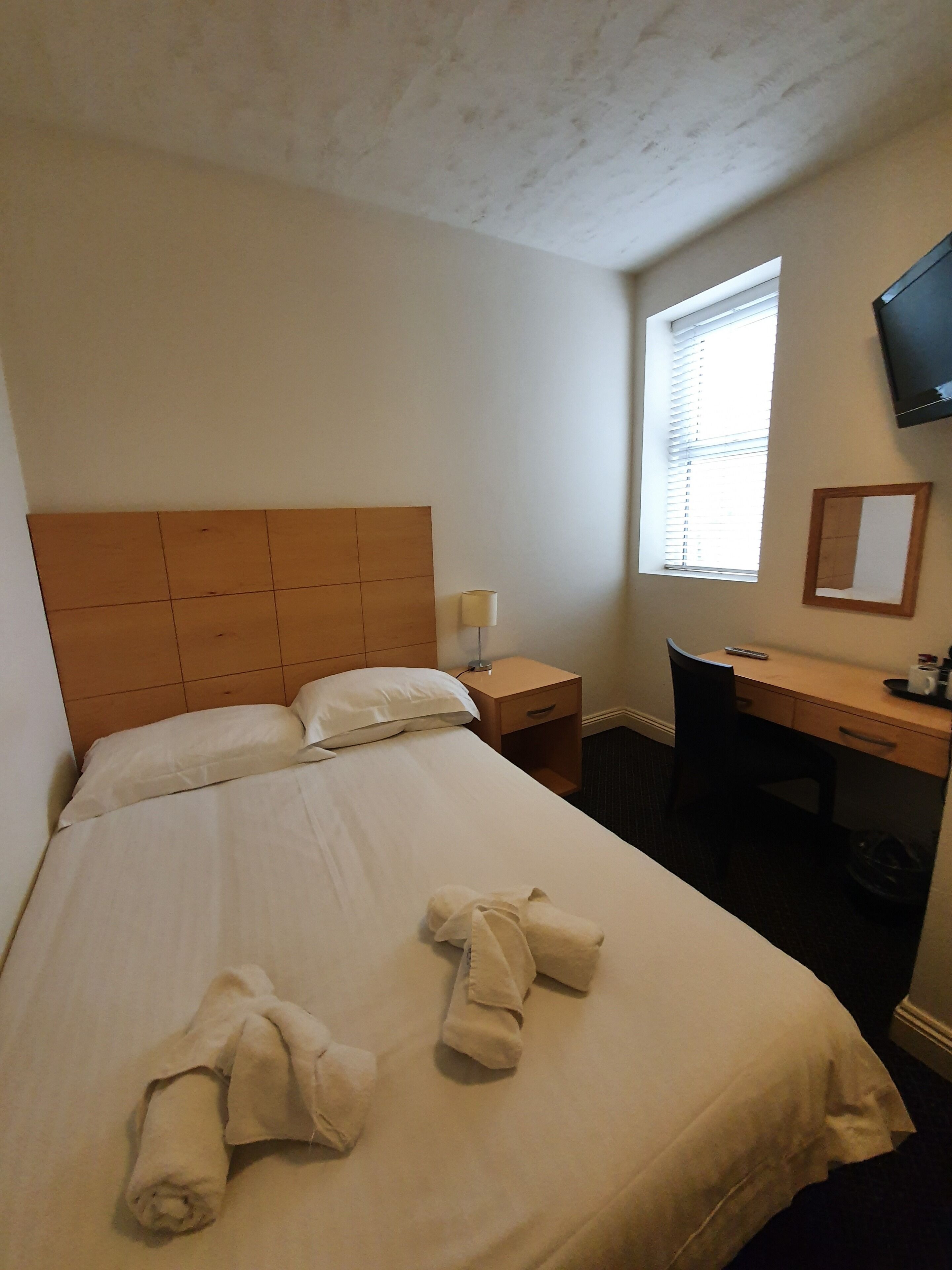 Une chambre d’hôtel avec un lit, un bureau, une chaise, une télévision et une fenêtre.