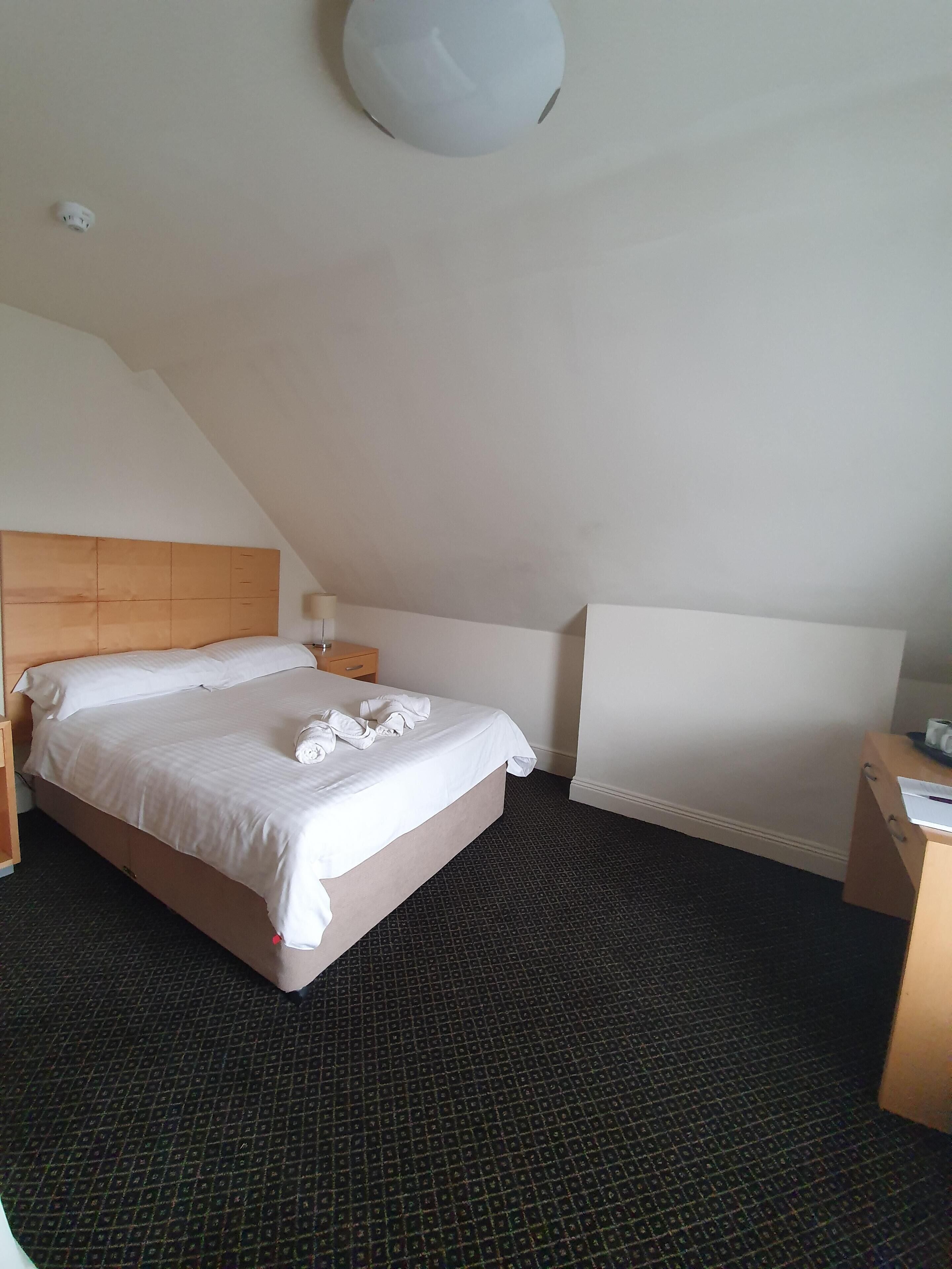 Quarto de hotel com cama, mesa de cabeceira, escrivaninha e luminária no teto.
