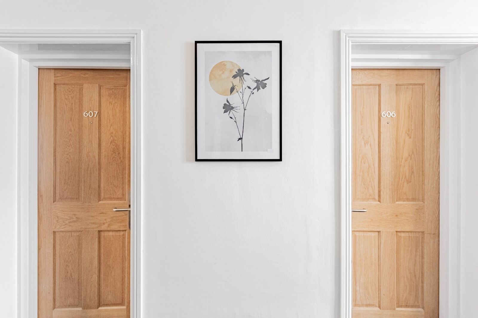 Two wooden doors with numbers 607 and 606, a framed artwork with a floral design, and a white wall.