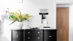 Un bureau en bois noir avec trois tiroirs, un vase blanc contenant des fleurs jaunes, un objet décoratif et un panneau indiquant qu’il faut composer le 0 pour joindre la réception.