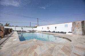 Una piscina con solárium de piedra, una pared blanca con un letrero azul y una pared de piedra con plantas.