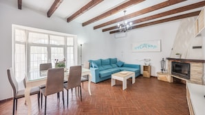 A living room with a blue sofa, wooden beams, a fireplace, and a dining area with chairs and a table. - Family Home "La Lobita 1" Short Drive from Beach with Pool, Terrace and Wi-Fi (Conil de la Frontera)