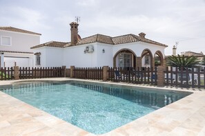 A swimming pool with a tiled deck, a white building with a tiled roof, and a wooden fence. - Family Home "La Lobita 1" Short Drive from Beach with Pool, Terrace and Wi-Fi (Conil de la Frontera)