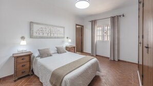 A bedroom with a bed, nightstands, a wall-mounted lamp, a door, and a window with curtains. - Family Home "La Lobita 1" Short Drive from Beach with Pool, Terrace and Wi-Fi (Conil de la Frontera)