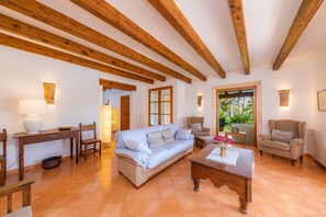 A room with wooden beams, a sofa, chairs, a table, and a view of greenery.