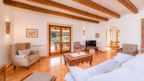 Una habitación con vigas de madera, un sofá, un televisor y un comedor con sillas.