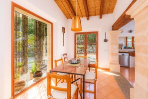 A dining area with a wooden table and chairs, a hanging pendant light, and a view of the outdoors through large windows.
