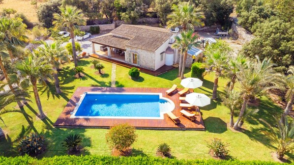 Une maison avec une piscine, entourée de palmiers et d’une pelouse bien entretenue.