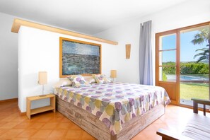 Une chambre à coucher avec un lit, des tables de chevet, un tableau, une fenêtre donnant sur un beau paysage et un banc.