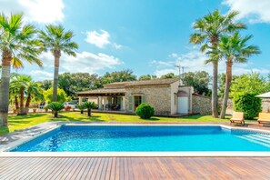 Une maison avec une piscine, entourée de palmiers et sous un ciel dégagé.