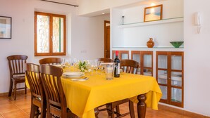 A dining area with a yellow tablecloth, wooden chairs, a wine bottle, and a vase on a shelf. - Country Estate with Pool, Wi-Fi, Air Conditioning, Garden and Patio (Artá)