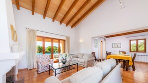 A spacious living area with a sofa, a dining table with yellow tablecloth, and a fireplace. - Country Estate with Pool, Wi-Fi, Air Conditioning, Garden and Patio (Artá)