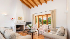 A living room with a fireplace, sofa, coffee table, and a view of the outdoors. - Country Estate with Pool, Wi-Fi, Air Conditioning, Garden and Patio (Artá)