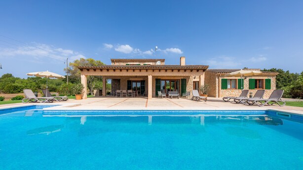 A poolside area with lounge chairs, a covered patio, and a stone building with a tiled roof. - Country Estate with Pool, Wi-Fi, Air Conditioning, Garden and Patio (Artá)