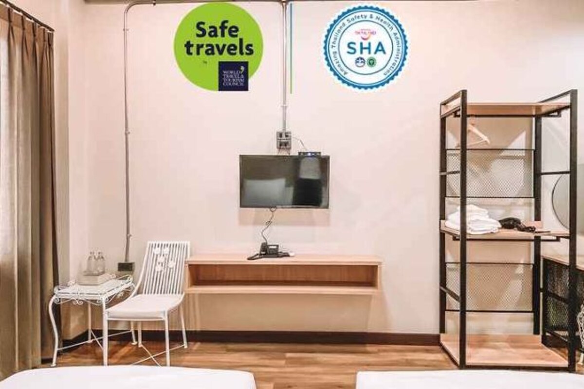Habitación de hotel con cama, escritorio con computadora, silla, televisor y estante con ropa.