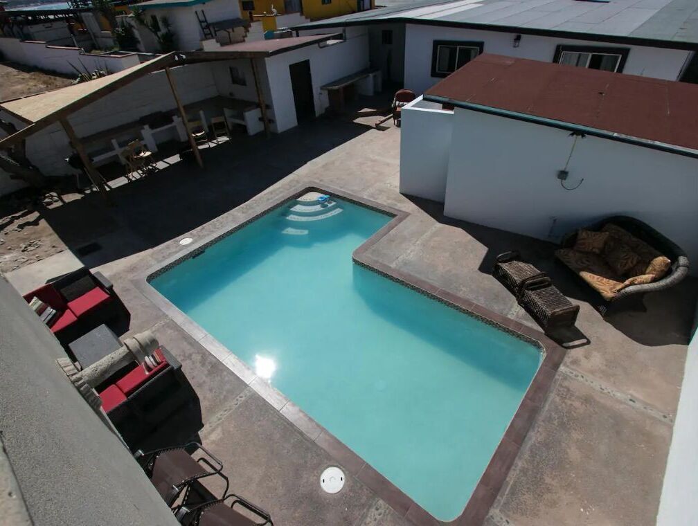 Et rektangulært pool med fliseterrasse, omgivet af liggestole og et lille bord.